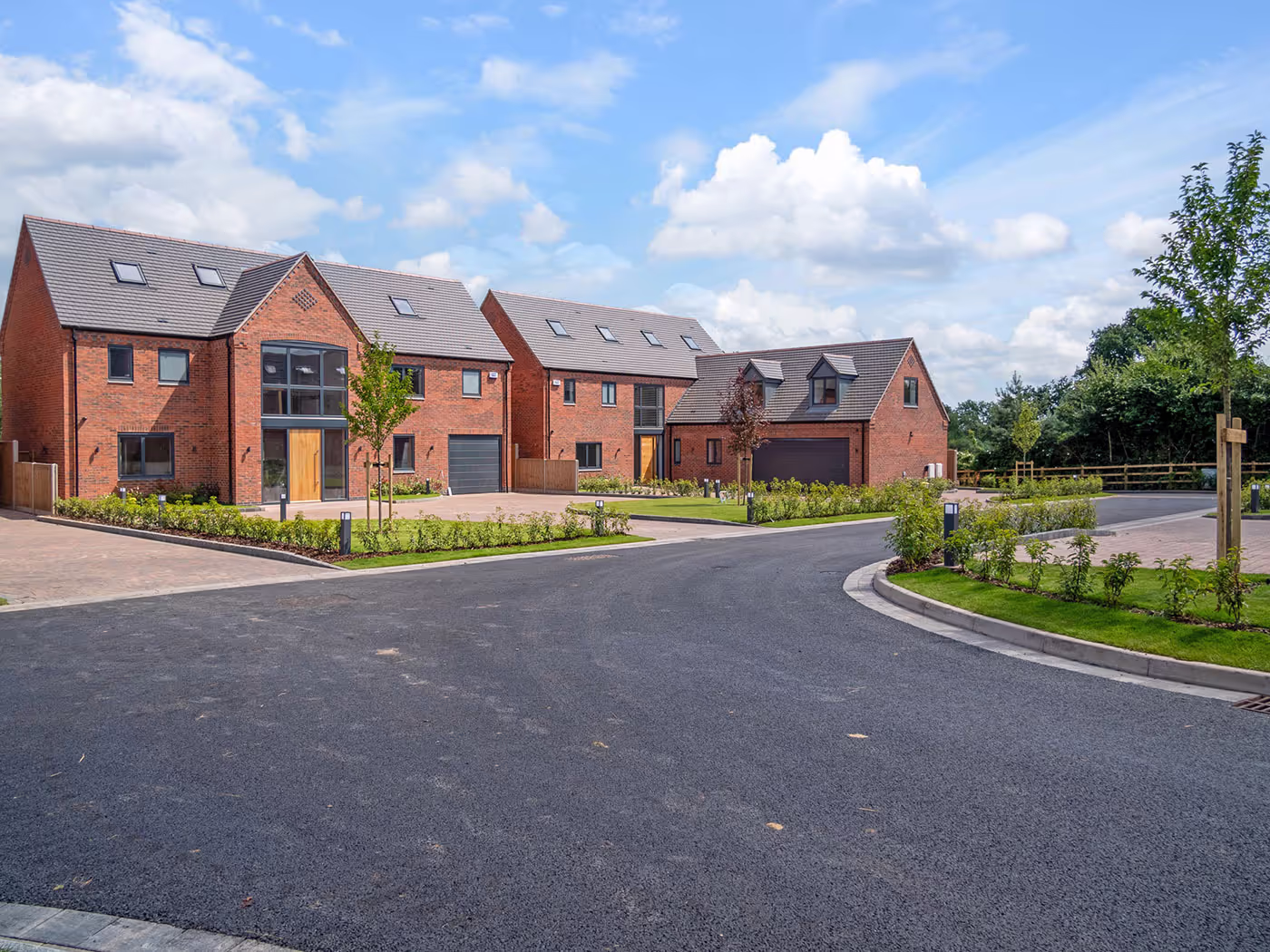 New brick houses with gray roofs, garages, and small front lawns on a curved paved street under blue sky.