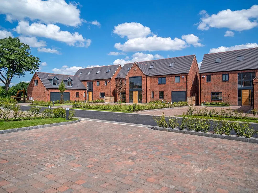 Newly built brick houses with dark roofs and garages under a partly cloudy blue sky.