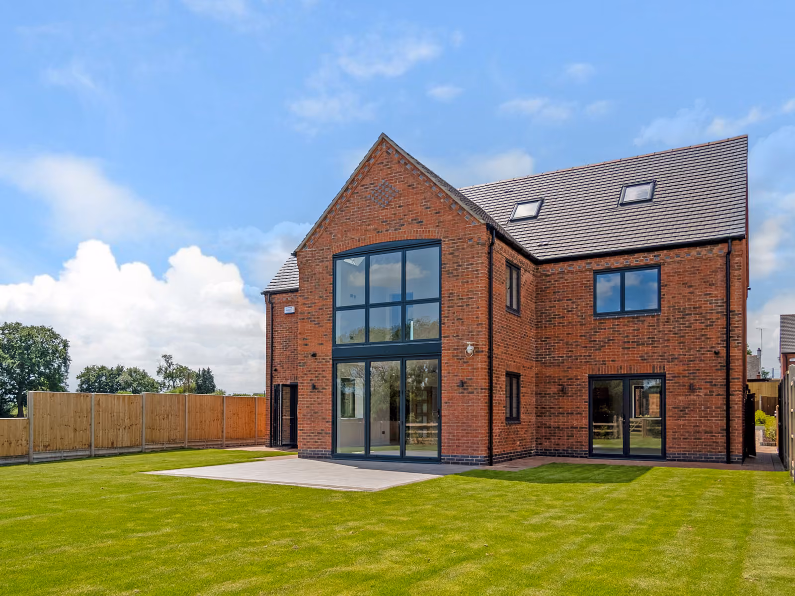 Modern two-story brick house with large windows and a spacious green lawn under a blue sky.