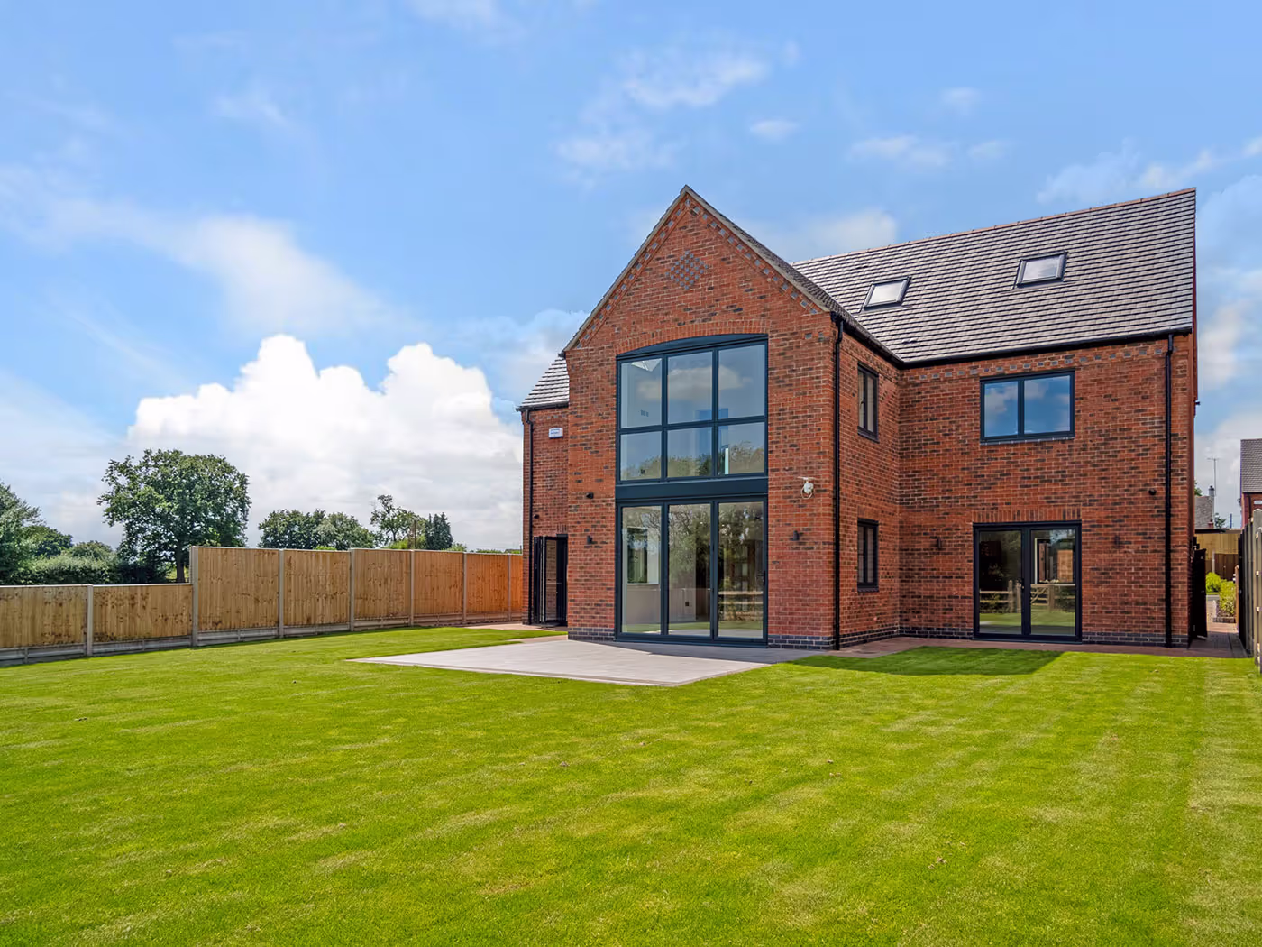 Modern two-story brick house with large windows and a spacious green lawn under a blue sky.