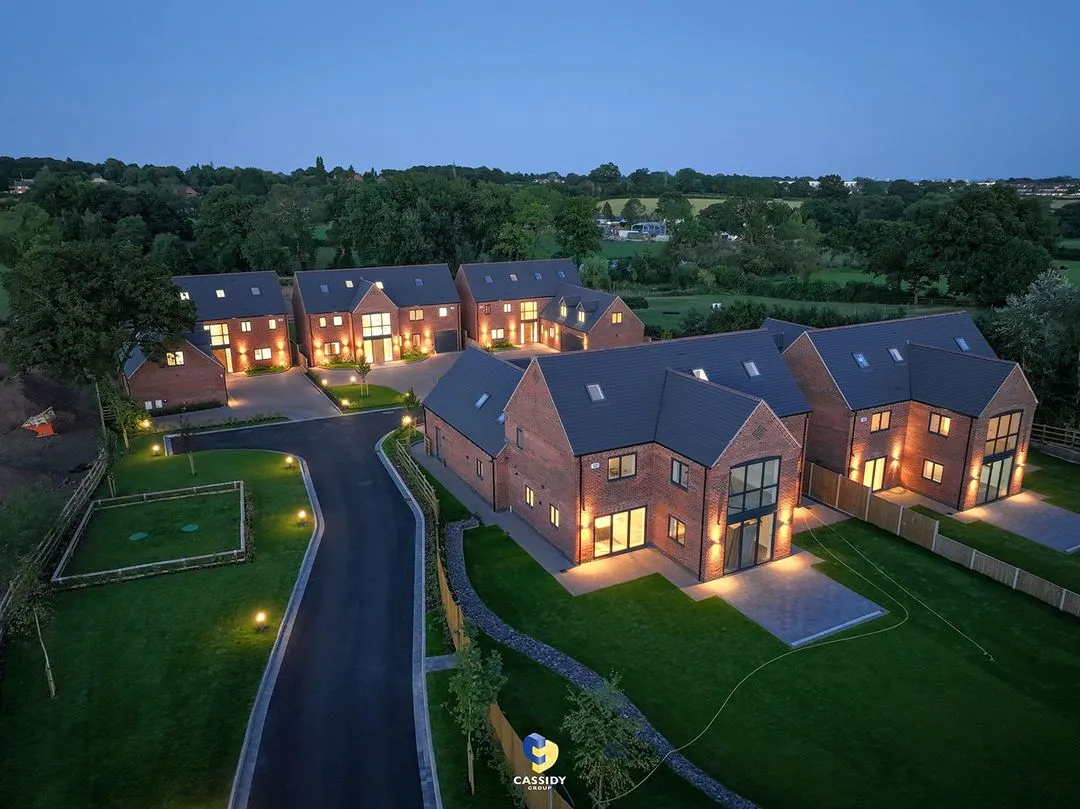 Night aerial view of a new residential neighborhood with lit brick houses and green lawns.