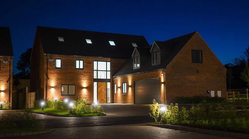 Night view of modern brick houses with illuminated windows, doors, and outdoor lighting.