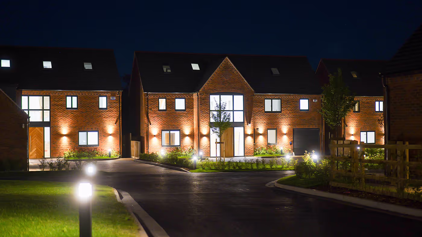 Night view of modern brick houses with illuminated windows, doors, and outdoor lighting.