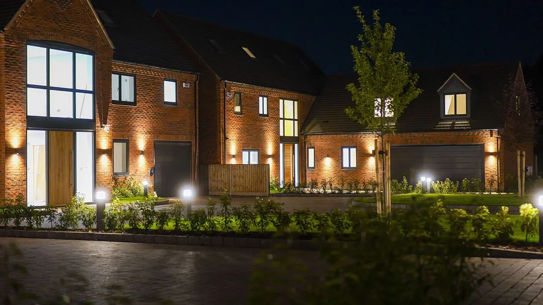 Night view of modern brick houses with illuminated windows, doors, and outdoor lighting.