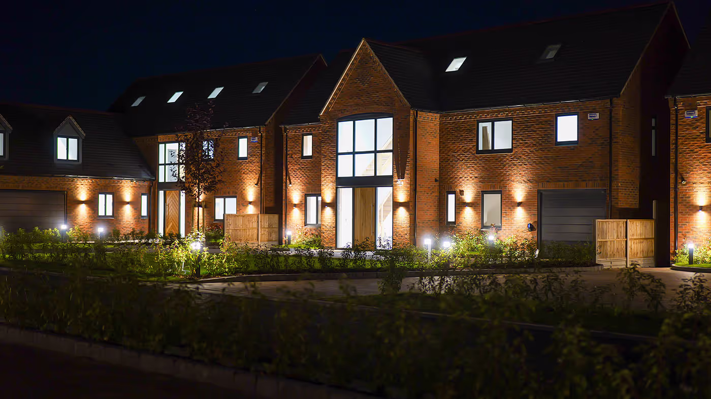 Night view of modern brick houses with illuminated windows, doors, and outdoor lighting.