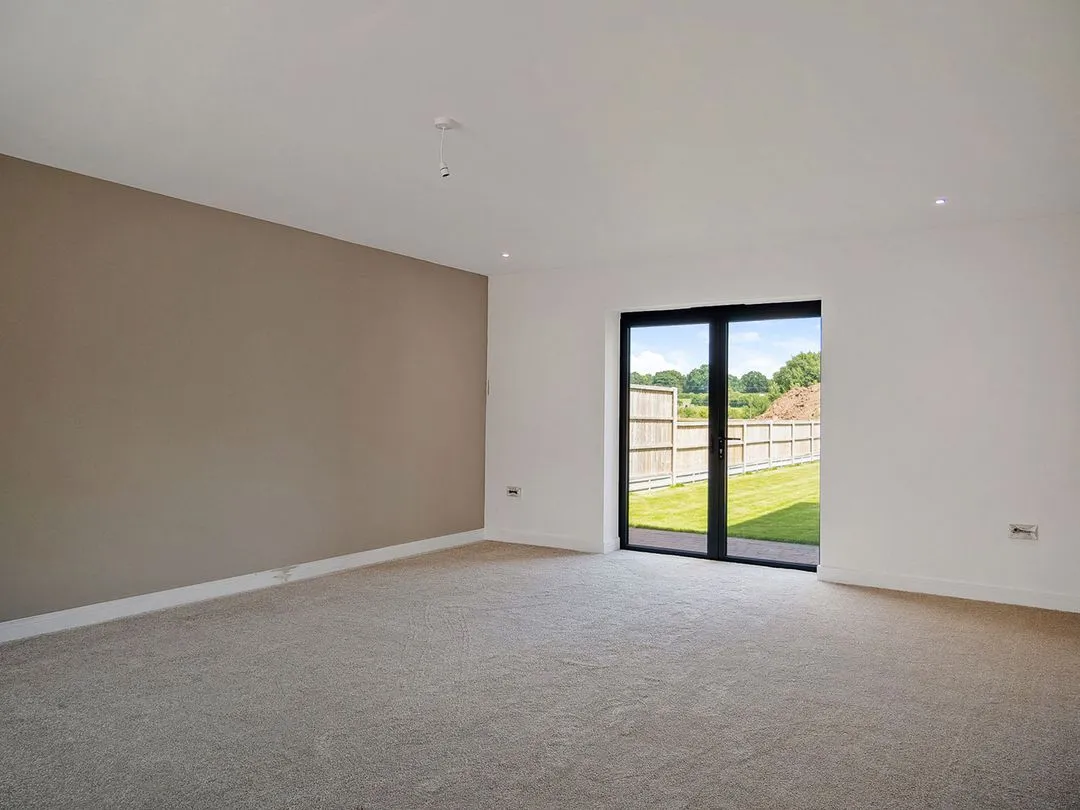 Empty room with beige carpet, tan accent wall, white walls, and glass doors opening to a fenced green yard.