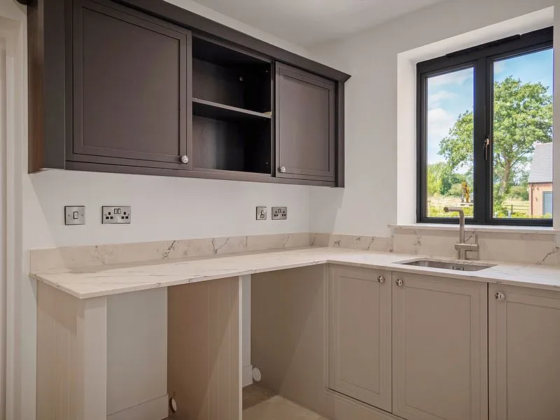 Modern kitchen corner with gray cabinets, marble countertop, stainless sink, and window showing greenery outside.