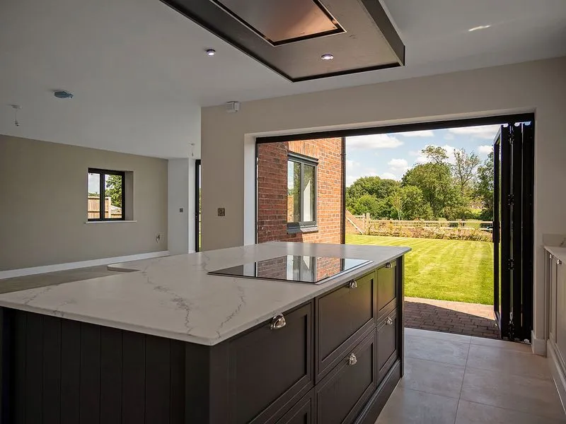 Modern kitchen island with marble countertop and stovetop facing large open doors to a green backyard.