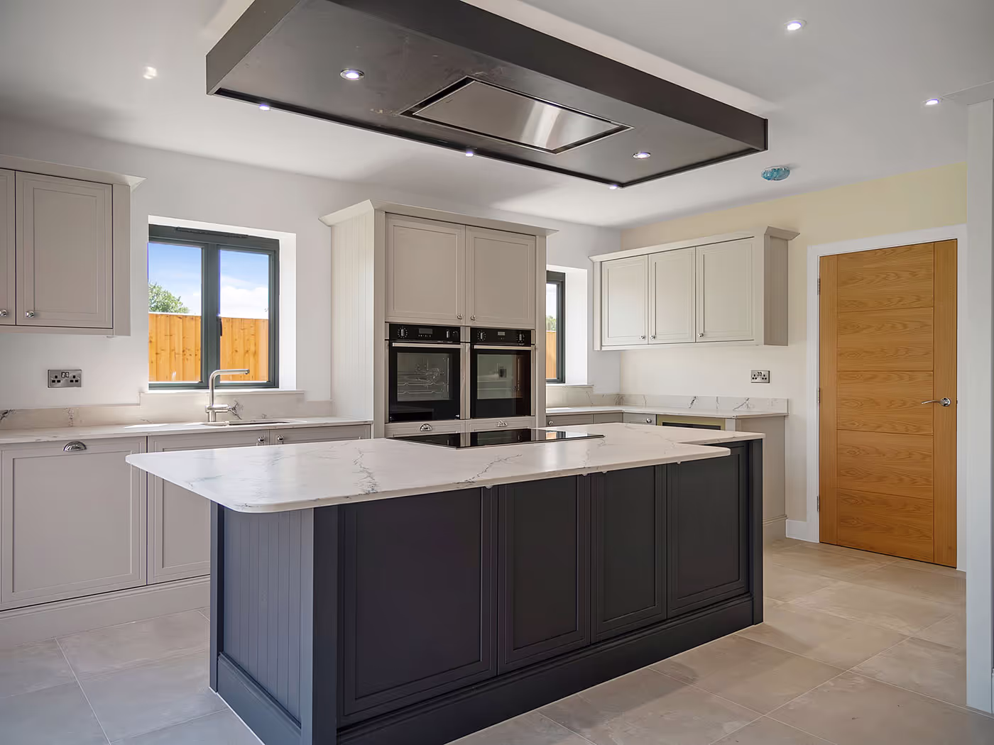 Modern kitchen with dark island, white marble countertop, built-in ovens, and light cabinetry.