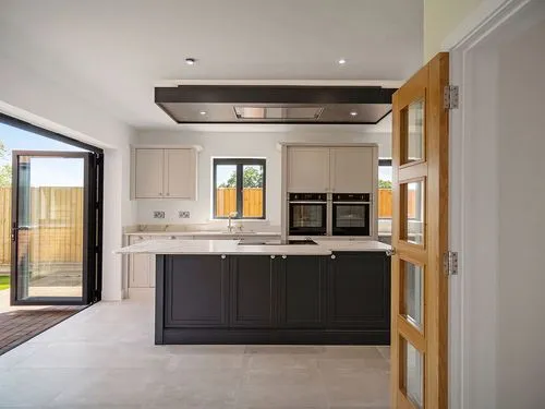 Modern kitchen with dark island, beige cabinets, built-in ovens, and open folding doors to outside.