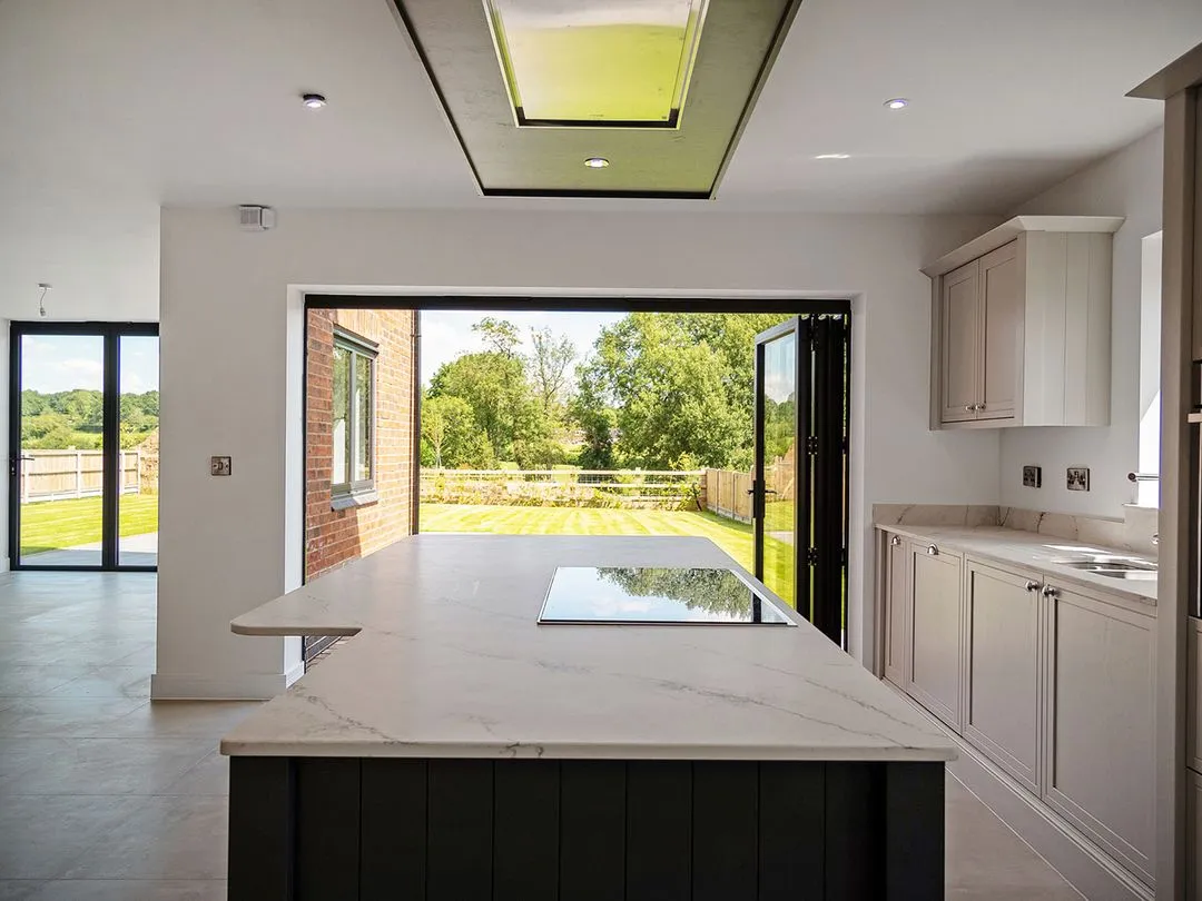 Modern kitchen with marble island, built-in stove, and bi-fold doors opening to a garden view.