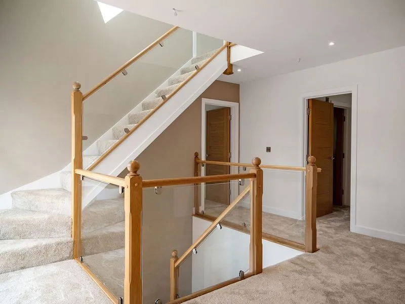 Carpeted staircase with wooden and glass railing in a bright, modern home interior with open doors.
