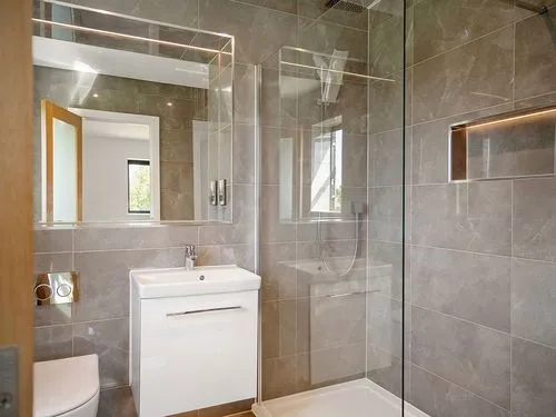 Modern bathroom with gray tiles, white vanity, glass shower, and a mirror above the sink.