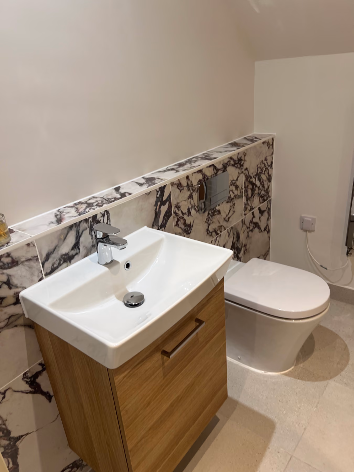 Modern bathroom with white sink on wooden cabinet and white toilet against marble-tiled wall.