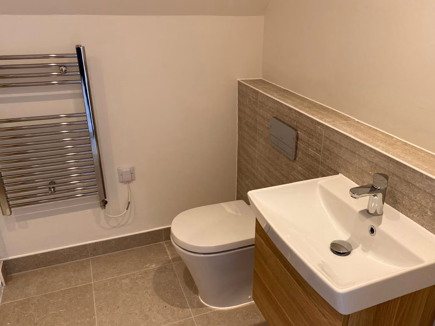 Modern bathroom with wall-mounted toilet, rectangular sink on wooden cabinet, and chrome towel radiator.