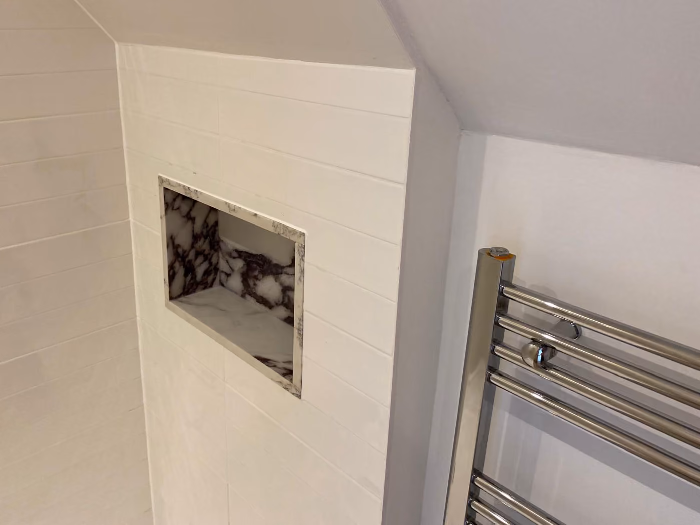 Bathroom wall with a recessed marble shelf niche and chrome towel radiator on the right.