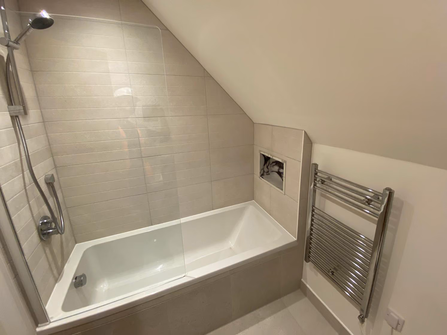 Modern white bathroom with built-in bathtub, glass shower screen, and chrome towel radiator.