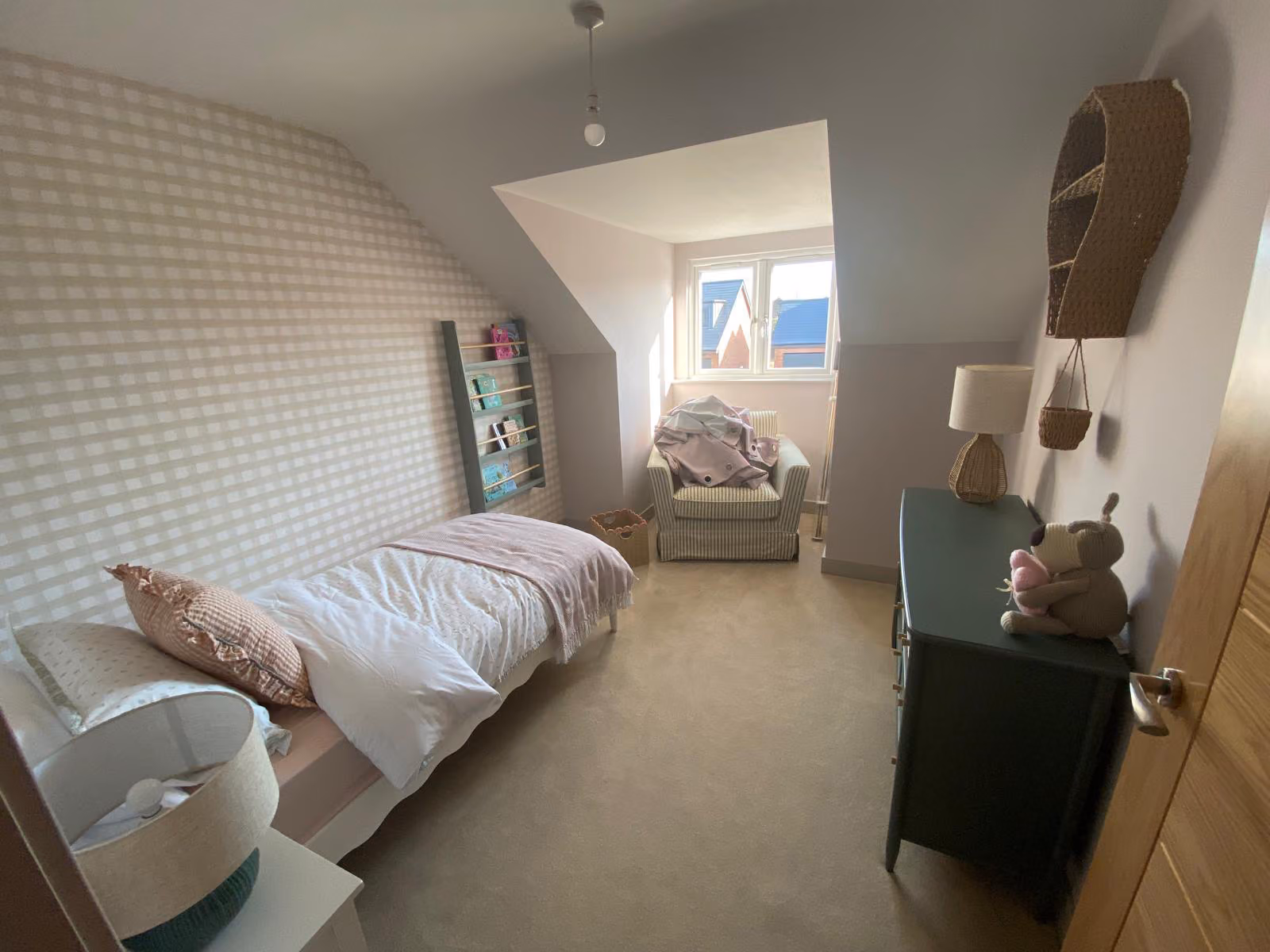 Small bedroom with a single bed, striped armchair by window, dark dresser, and toys on dresser.