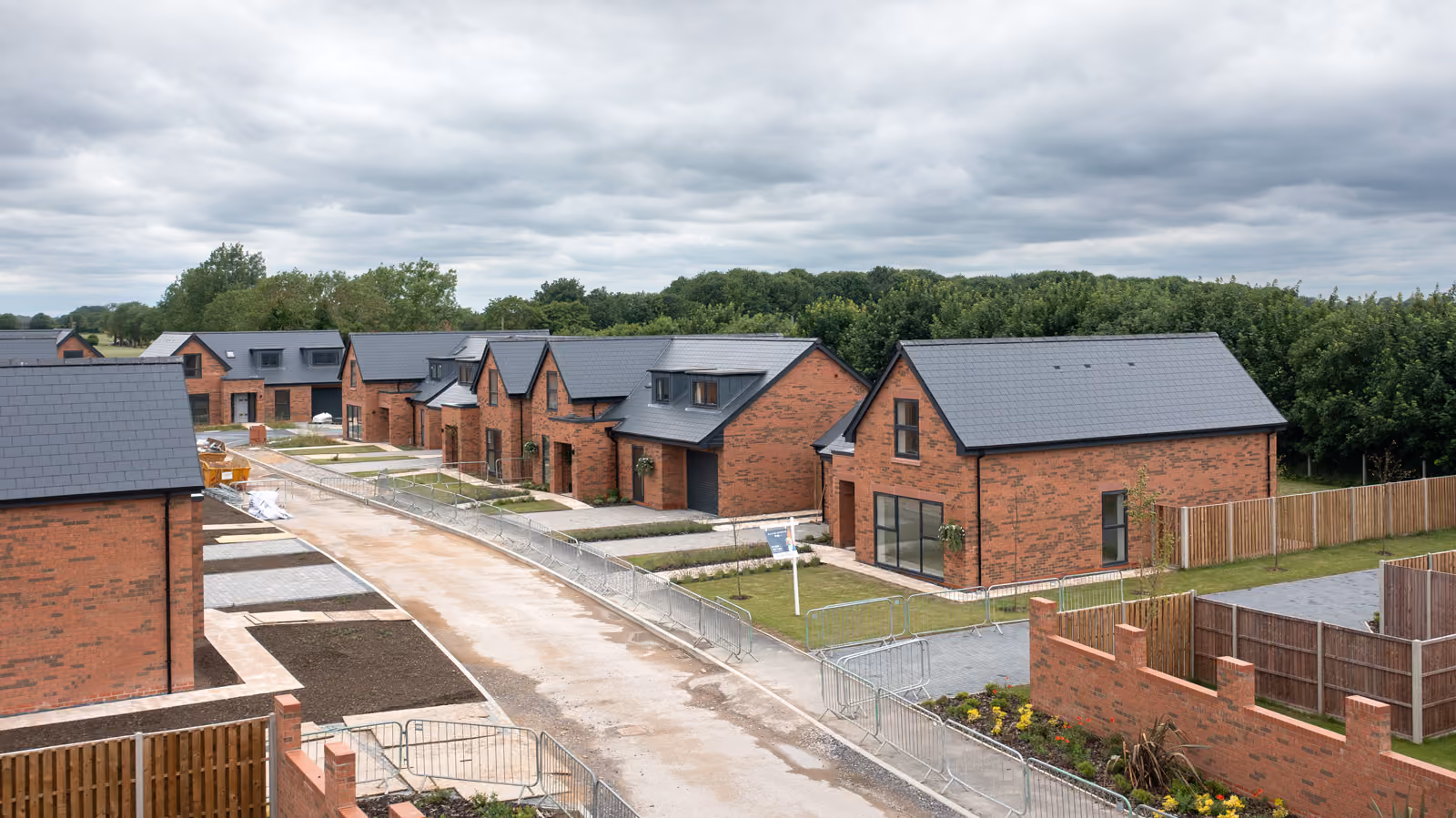 Aerial view of new brick houses with dark roofs along a curved street under cloudy sky.