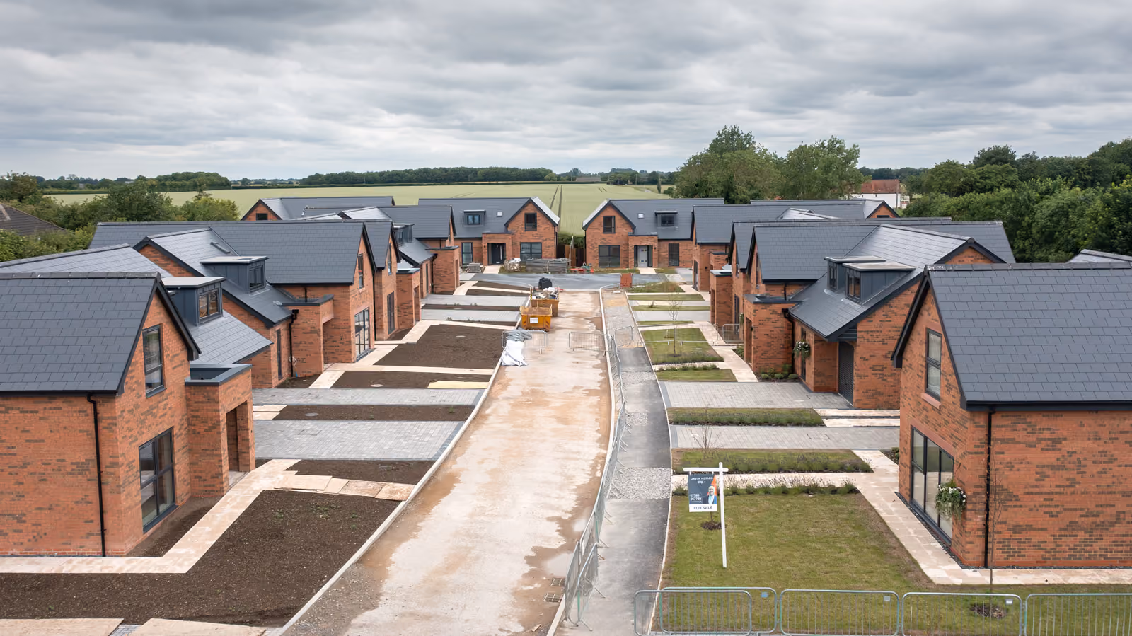 Aerial view of newly built brick houses with gray roofs on a cloudy day in a rural area.