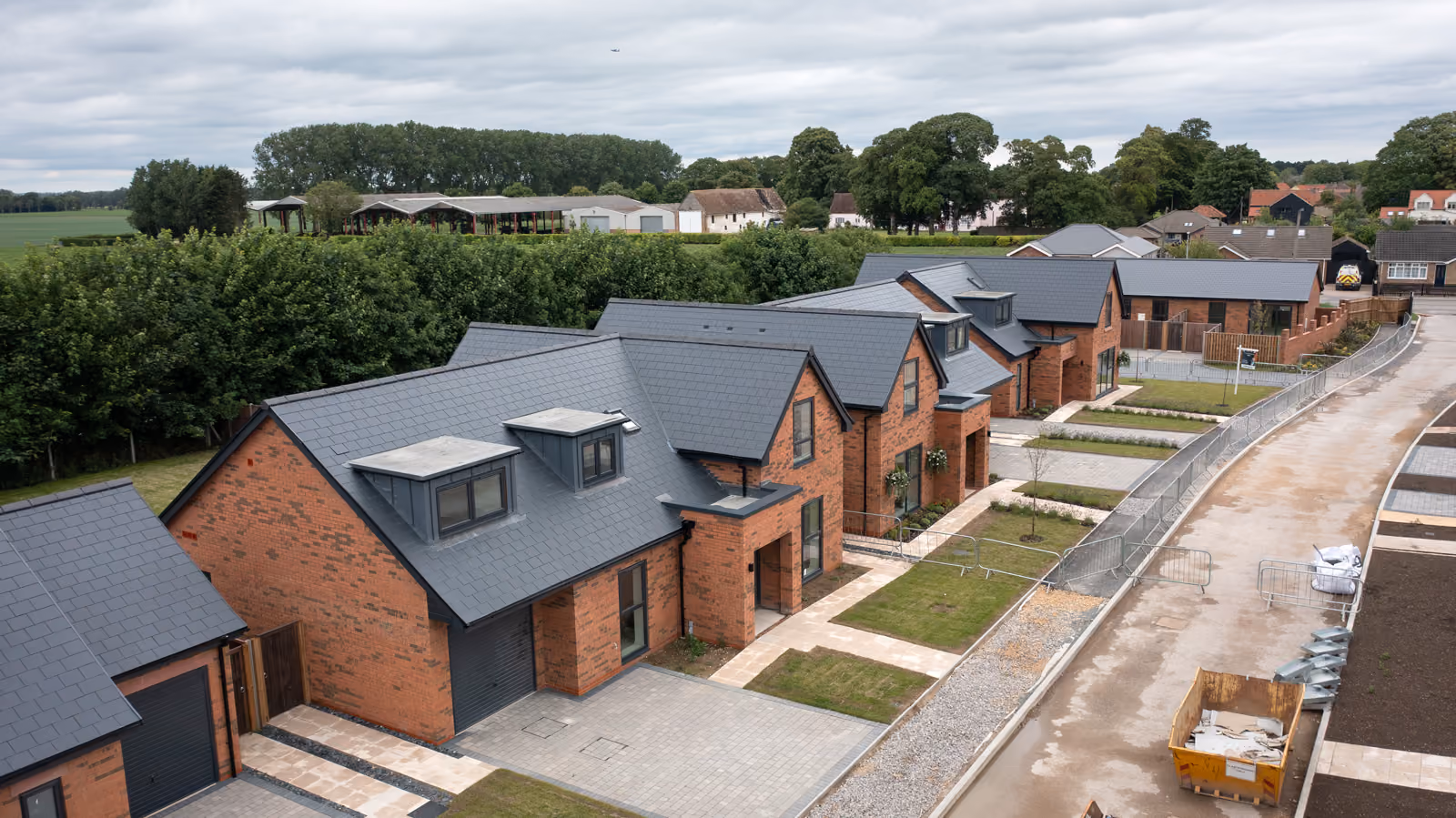 Row of modern brick houses with gray roofs along a street under cloudy sky.