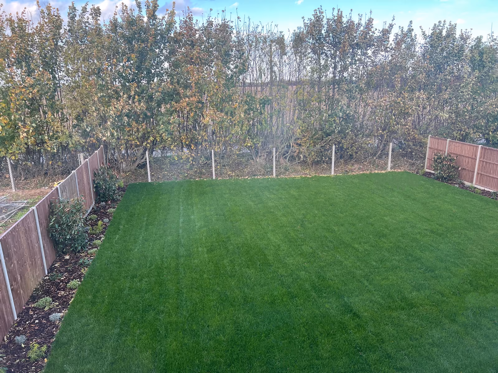 Well-kept rectangular green lawn bordered by wooden fences and trees under blue sky.