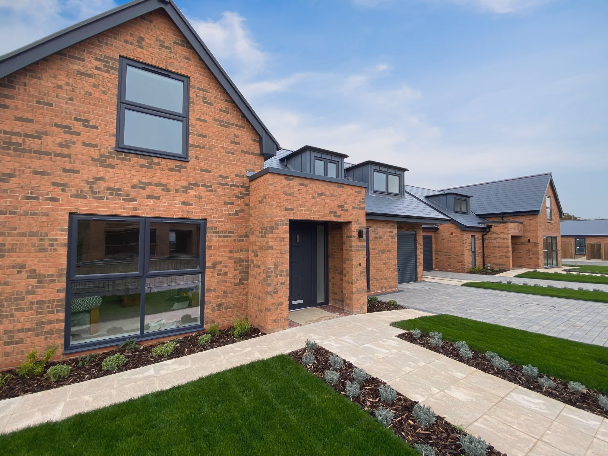 Modern brick houses with black framed windows, dark front doors, and neat lawns under a blue sky.