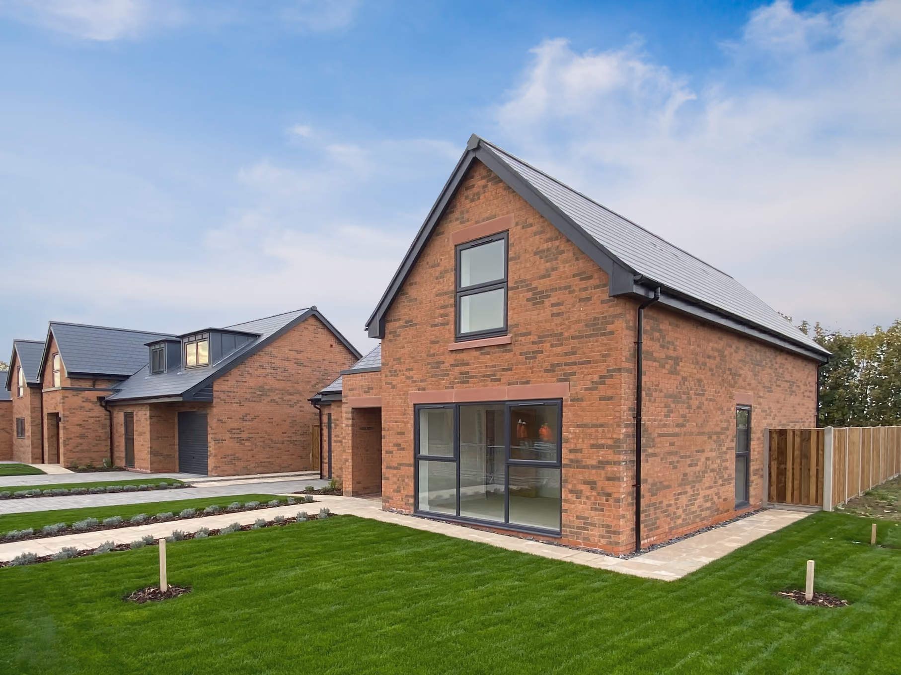 New brick houses with gray roofs, large windows, and neatly trimmed green lawns under a blue sky.