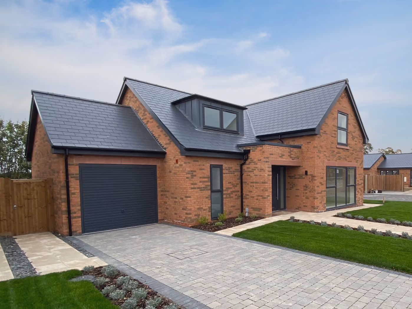 Modern brick house with dark garage door, large front windows, slate roof, and green lawn.