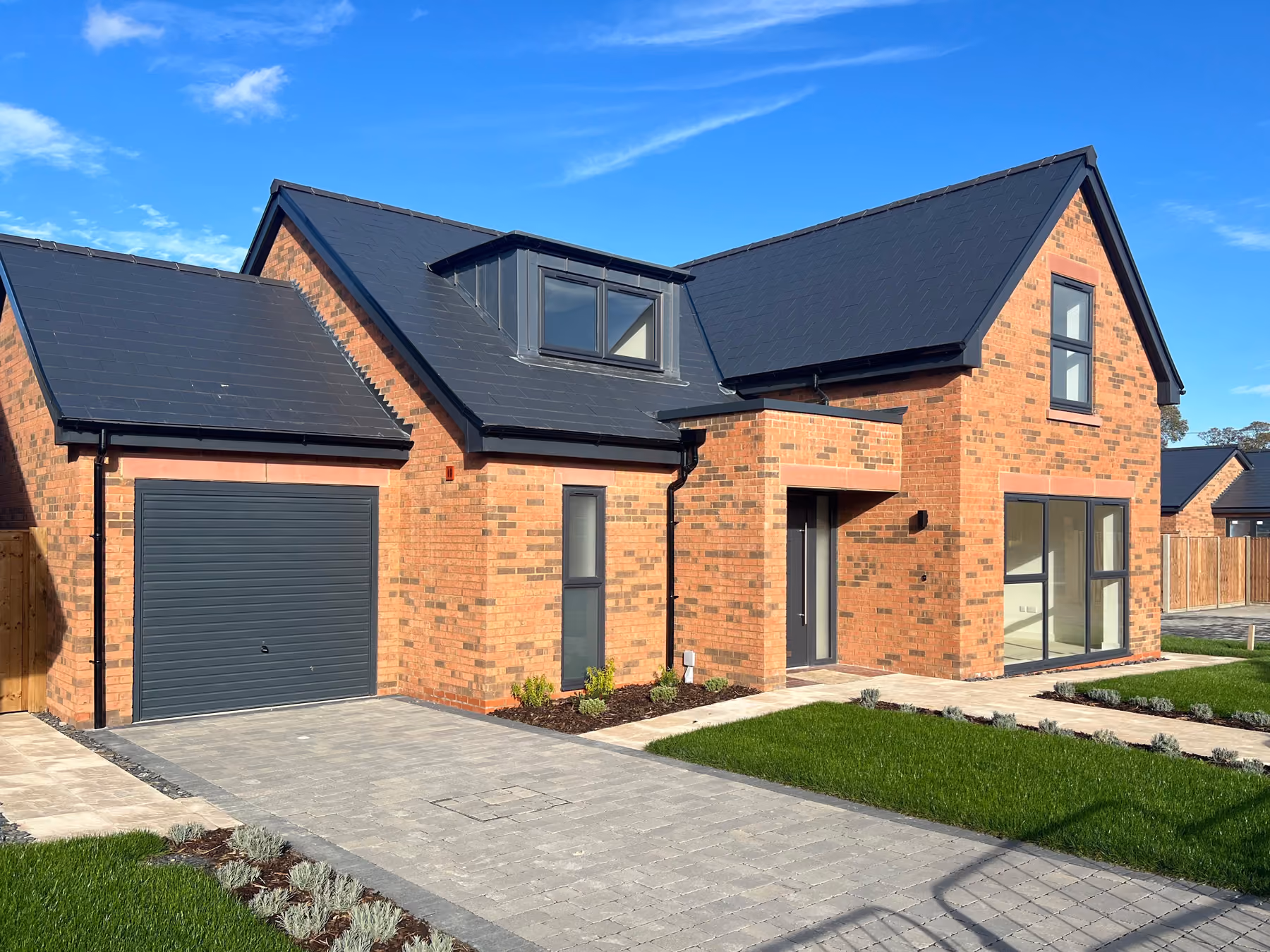 Modern brick house with black roof, large garage, front door, windows, and paved driveway under blue sky.
