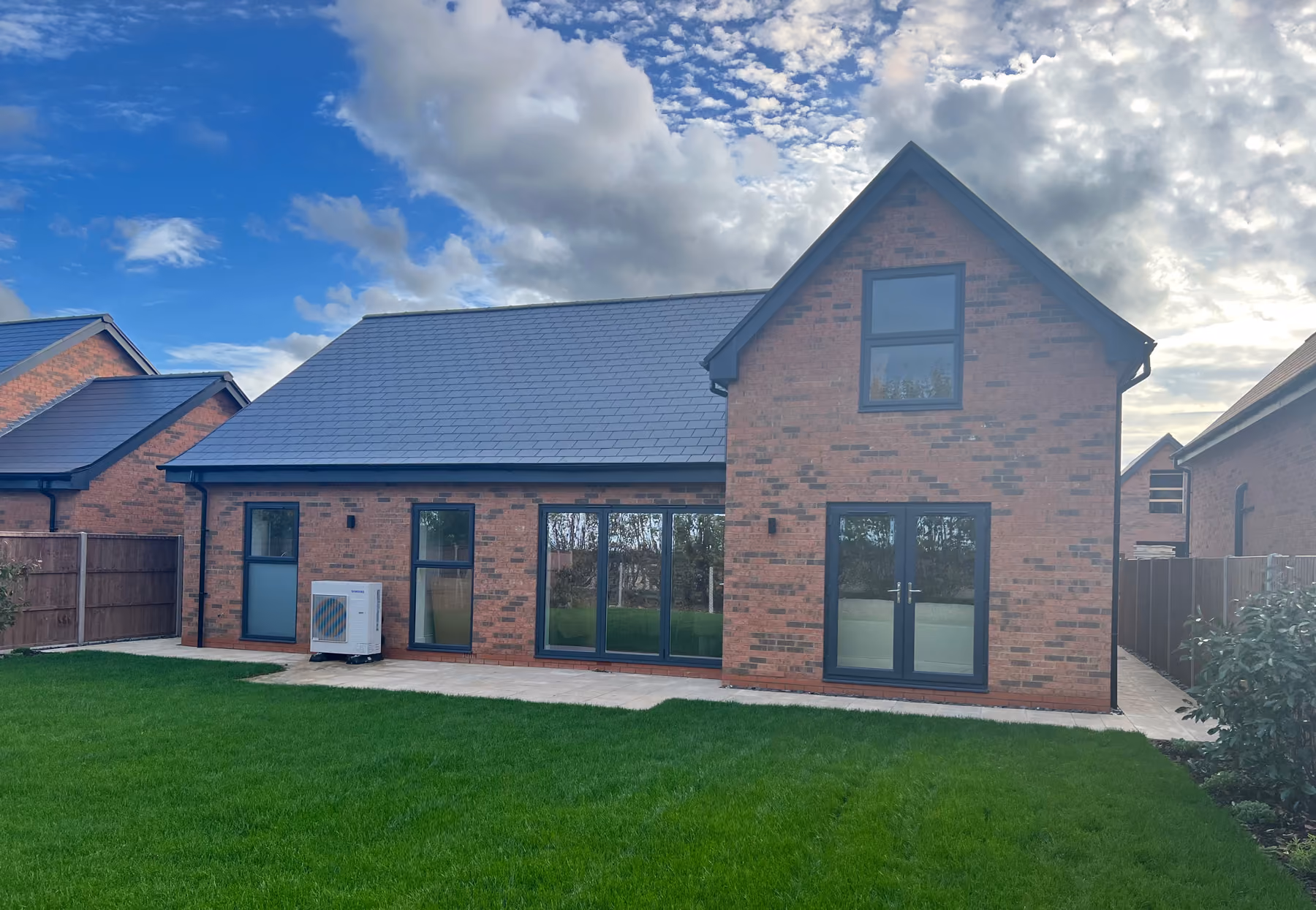 Modern brick house with black window frames, glass doors, and a green lawn under a partly cloudy sky.