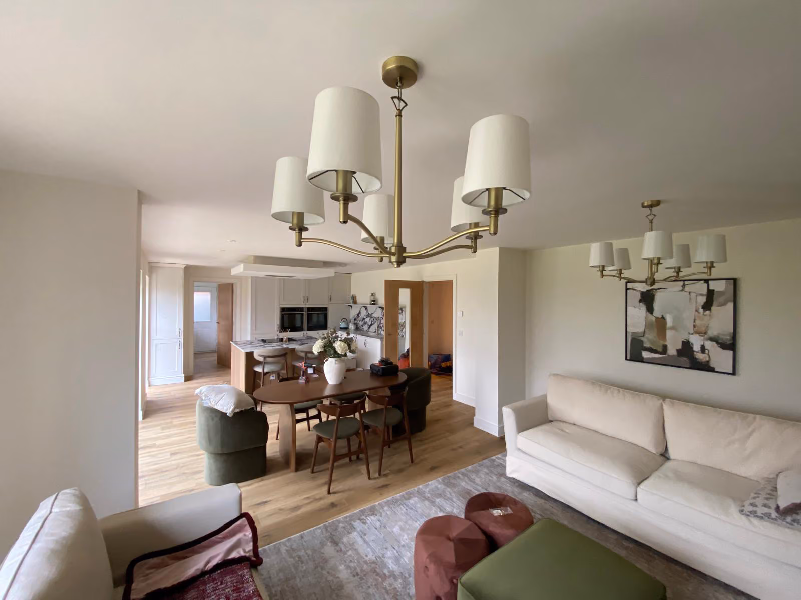 Modern open living room with beige sofa, green chair, wooden dining table, and kitchen in background.