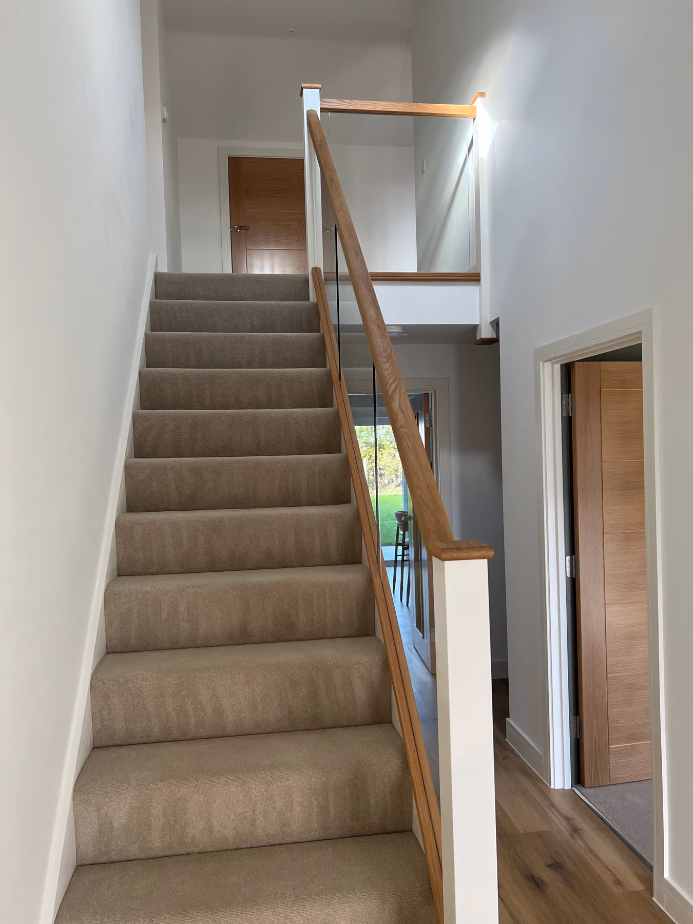 Carpeted staircase with wooden handrail and glass panel leading to a closed wooden door at the top.