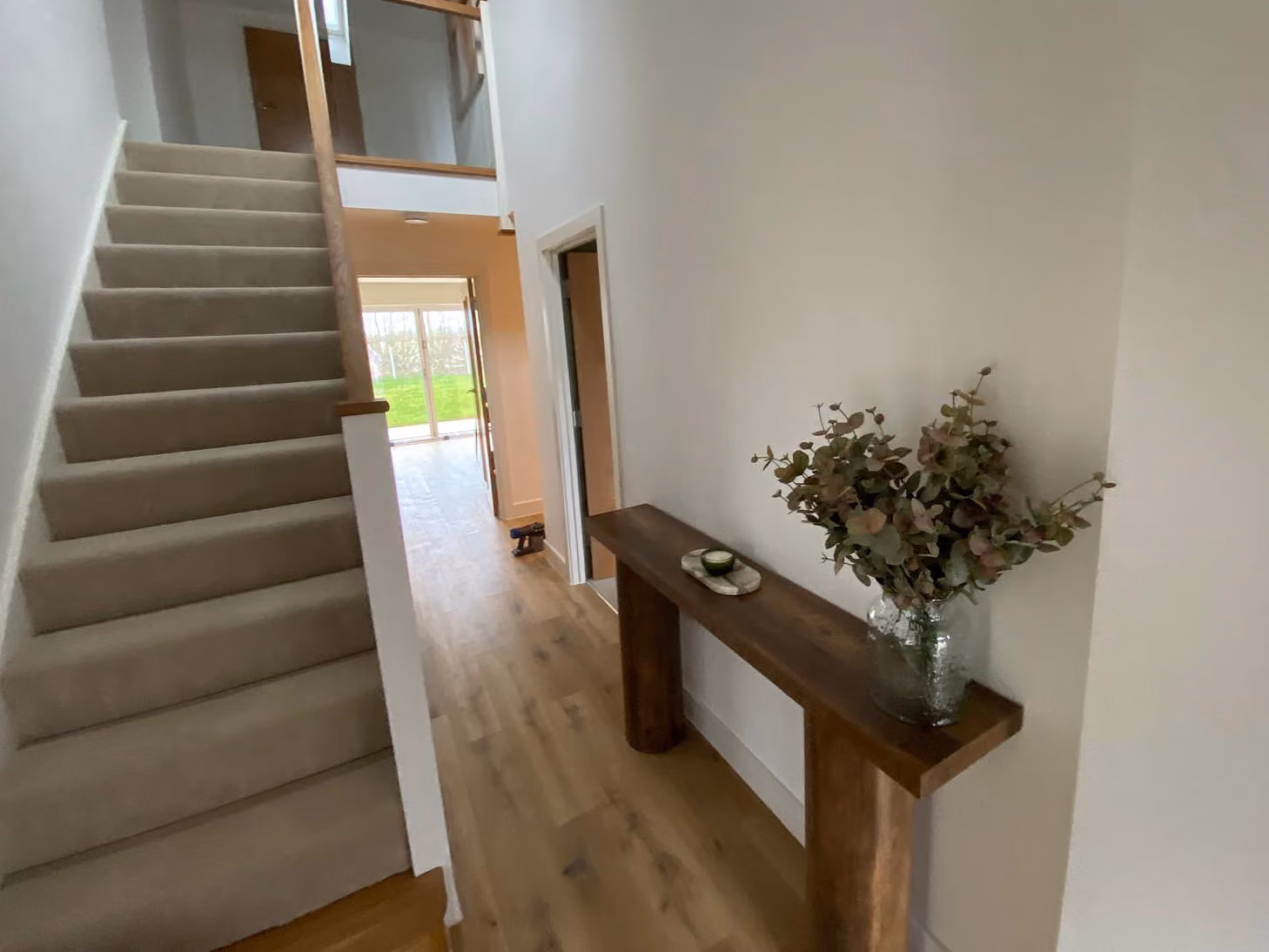 Entryway with carpeted stairs on left, wooden floor, and console table with a vase of foliage on right.