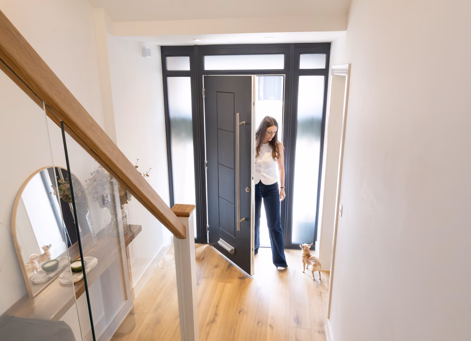 Rosey Cassidy opening black front door in a bright entryway with a small dog looking up at her.